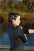A woman is stretching outdoors by a body of water, wearing earbuds. Anteprima dell’immagine prodotto