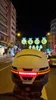 A person wearing a helmet with integrated lights on a city street at night, with Christmas decorations in the background. Náhled obrázku produktu