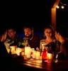 A group of people are sitting around a table at night, illuminated by candles. Podgląd zdjęcia produktu