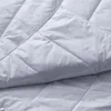 A close-up, angled view of a white quilted blanket. Produktbild-Vorschau