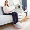 A woman is sitting on a couch reading a book while her feet are in a heated foot warmer. Produktbild-Vorschau