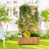 A wooden planter box with a trellis, filled with plants and flowers, sits in a garden in front of a white house. Podgląd zdjęcia produktu