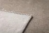 A close-up view of a light gray blanket with a stitched gray border, placed on a textured gray surface. Produktbild-Vorschau