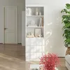 A white bookshelf with drawers and decorative items on shelves, placed in a room with a door and a plant. Produktbild-Vorschau