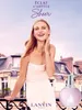A woman is posing on a balcony with a perfume bottle in front of a Parisian building. Podgląd zdjęcia produktu