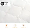 A close-up of quilted white fabric, likely a mattress topper or duvet, with several certification and information icons at the bottom. Produktbild-Vorschau