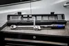 A torque wrench and socket set are laid out on a black surface in front of a car door. Anteprima dell’immagine prodotto