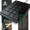 A woman is working on a laptop in a dimly lit room with plants, while a product image of a black numpad is overlaid. Voir les images du produit