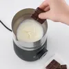 A hand is holding a piece of chocolate over a milk frother filled with milk. Produktbild-Vorschau