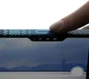 A finger is pressing a button on a phone case with a carbon fiber pattern. The phone screen shows a landscape with mountains and a city skyline. Podgląd zdjęcia produktu