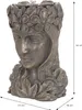 A bronze-colored planter shaped like a woman's head, adorned with flowers and leaves, with dimensions indicated. Náhled obrázku produktu