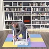 A man is assembling a white furniture piece on a colorful puzzle mat in front of a large bookshelf. Voir les images du produit