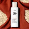A bottle of Anua Rice 70 Intensive Moisturizing Milk is placed on a textured brown fabric, surrounded by rice grains. Produktbild-Vorschau