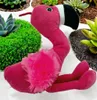 A plush flamingo toy is placed among succulents and moss. Produktbild-Vorschau