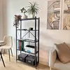 A black metal shelving unit with five shelves, containing books, binders, a printer, and decorative plants, is placed in a room with a chair and a sofa. Artwork hangs on the wall. Voir les images du produit
