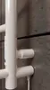 A close-up view of a white electric towel radiator mounted on a gray tiled wall. Náhľad obrázku produktu