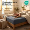 A woman sleeping peacefully on a bed with a dark gray fitted sheet, in a well-lit bedroom. Produktbild-Vorschau