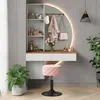 A vanity table with a mirror, stool, and decorative items, set in a room with plants. Voir les images du produit