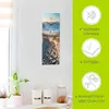 A vertical clock with a beach scene image is mounted on a white wall. To the right of the clock, there is a green panel with icons and text describing product features. Below the clock, on a white shelf, are several kitchen canisters and a plant. Produktbild-Vorschau