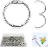 A collection of silver binder rings in a clear plastic container, with a single open binder ring and a close-up of a binder ring attached to a small notebook with a floral illustration. Produktbild-Vorschau