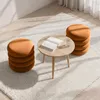 A round coffee table with a book and a glass of water, next to a stack of orange ottomans on a fluffy white rug. Podgląd zdjęcia produktu