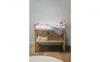 A wooden baby changing table with a mattress and bedding, a basket of items, and a pink toy. Produktbild-Vorschau