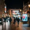A nighttime street scene in a city with people walking and cars driving. Produktbild-Vorschau