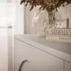 A close-up view of a white TV board with a vase of dried flowers and two books on top. Produktbild-Vorschau