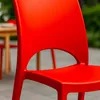 A close-up shot of a red plastic chair, likely for outdoor use, with a blurred background of a table and greenery. Produktbild-Vorschau