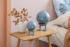 Two decorative figures are placed on a wooden side table next to a vase with dried leaves and a bed. Produktbild-Vorschau