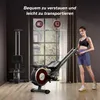 A woman is standing next to a rowing machine in a room with a large window. Produktbild-Vorschau