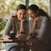 Two women laughing while looking at a smartphone in a cafe. Produktbild-Vorschau