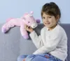 A young girl sitting on a couch, holding a pink unicorn plush toy. Produktbild-Vorschau