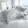 A bed with white and gray bedding featuring a green Christmas tree and snowflake pattern, set in a bright room with a large window. Produktbild-Vorschau