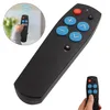 A hand holding a black remote control with blue and red buttons, with a circular inset showing a person using a similar remote. Produktbild-Vorschau