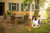 A woman reads a book in a hanging chair in a garden, with a cat looking up at her. Náhled obrázku produktu