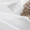 A close-up view of white sheer fabric with brown leaf embroidery. Produktbild-Vorschau