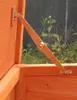 Close-up of a hinge mechanism on an orange wooden structure, likely a pet house or storage box, with greenery in the background. Produktbild-Vorschau