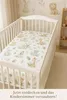 A crib with a fitted sheet featuring a jungle animal print. Produktbild-Vorschau