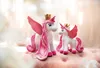 Two plush unicorns with pink wings and manes, wearing gold crowns, are sitting on a pink surface. Produktbild-Vorschau