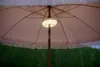 The underside of a pink patio umbrella with a built-in light, set against a green hedge. Produktbild-Vorschau