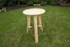 A wooden high table is set up on a green lawn with bushes in the background. Produktbild-Vorschau