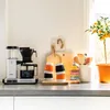 A coffee maker and kitchen accessories are displayed on a countertop next to a window. Náhľad obrázku produktu