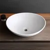 A white ceramic sink sits on a wooden surface, with a small black container to the left. Produktbild-Vorschau