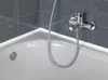 A close-up view of a white bathtub with a chrome faucet and shower hose attached to a dark tiled wall. Náhled obrázku produktu