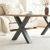 A close-up view of a coffee table with a wooden top and black metal legs, placed on a white rug in a living room setting. A white sofa and a decorative pillow are visible in the background. Podgląd zdjęcia produktu