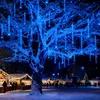 A snowy Christmas market at night, with a large tree decorated with blue icicle lights in the foreground. Produktbild-Vorschau