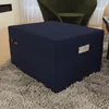 A dark blue ottoman is placed on a fluffy gray rug in a living room setting. A green chair is visible in the background. Produktbild-Vorschau