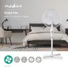 A bedroom scene with a stand fan in the foreground, next to a bed and a desk. Podgląd zdjęcia produktu
