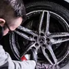 A person is cleaning a car wheel with a spray bottle. Produktbild-Vorschau